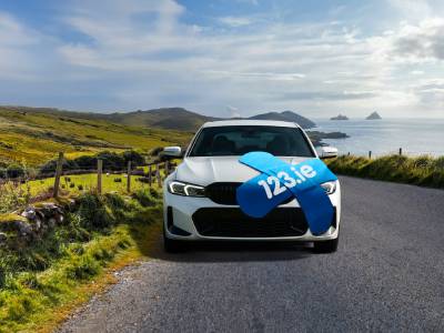 A car on a country road, featuring a blue 123.ie "cover that sticks" bandage logo on the top.